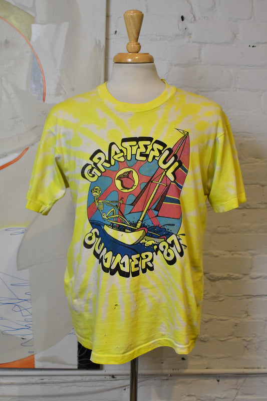 Yellow tie-dye t-shirt with a graphic design on a mannequin against a white brick wall.